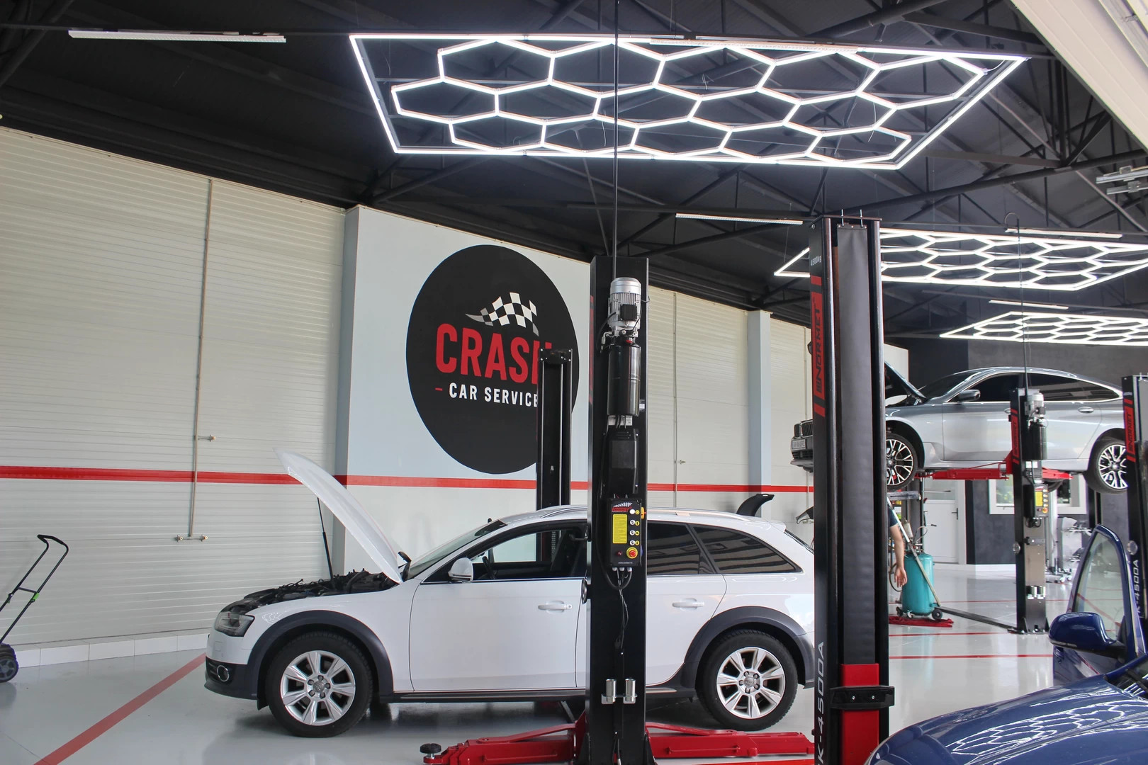 Auto servisná dielňa s bielym vozidlom na zdviháku, LED hexagonovým osvetlením a logom CRASH.