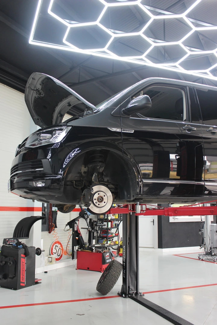 Čierne auto zdvihnuté na servisnom stojane, otvorené predné koleso a mechanici v dielni.