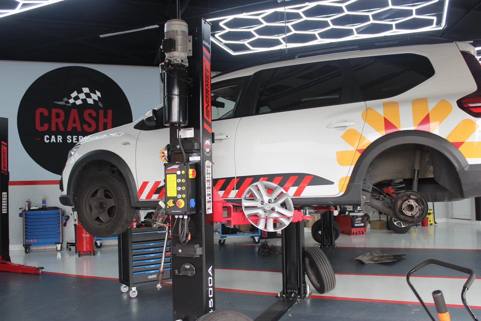 Biele firemné auto s logom na dverách zdvihnuté na hydraulickom zdviháku
